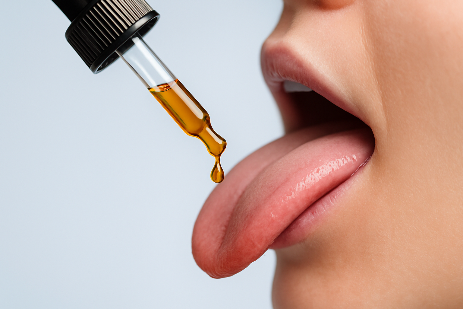 closeup photo of an herbal liquid being droppered out of a dropper onto a tongue, against a light blue background